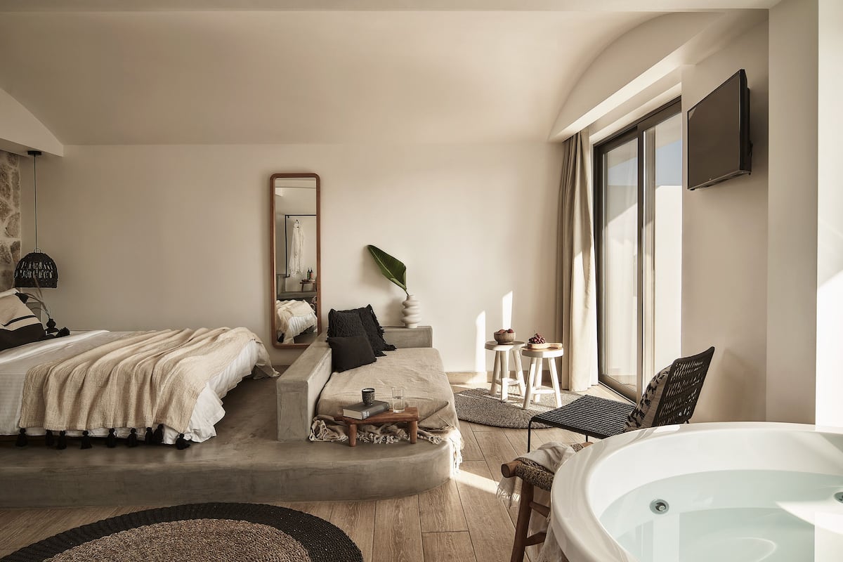 Un dormitorio moderno con una cama grande, un sofá, una mesita, una silla, una bañera y un ventanal amplio.