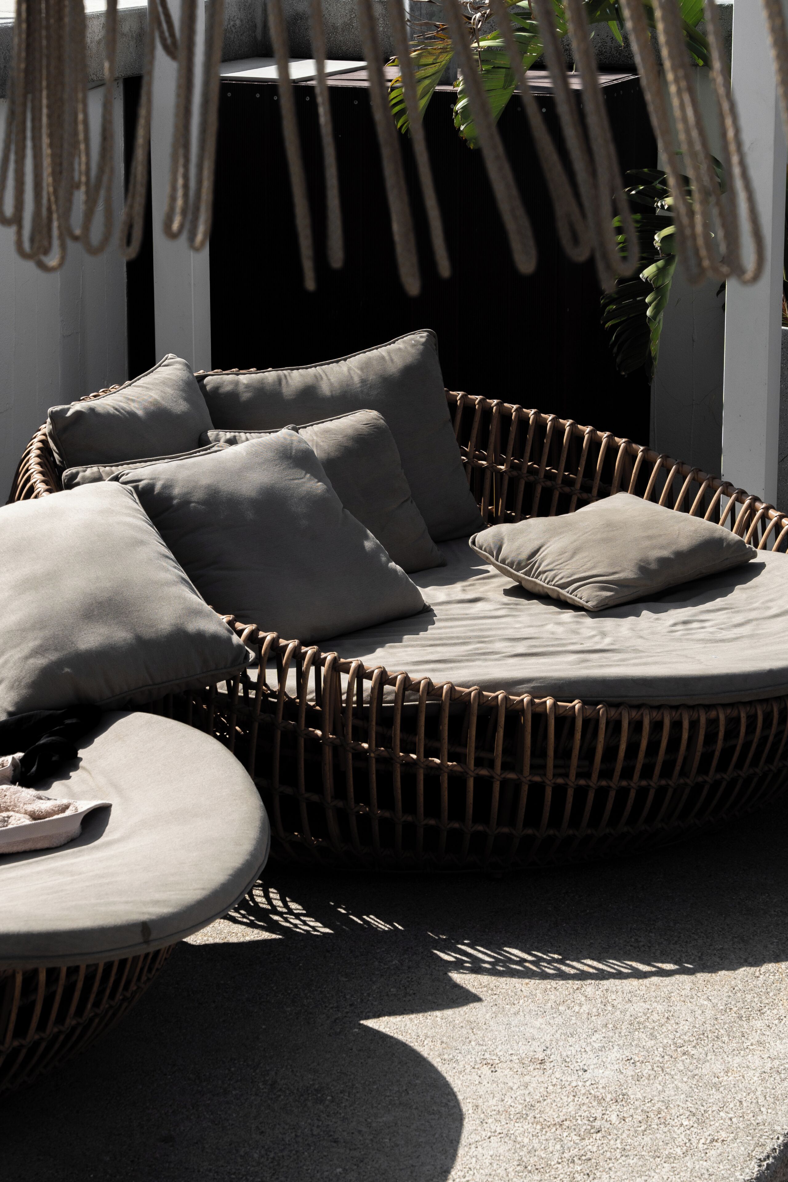 Een terras met wicker meubels, kussens en een ronde tafel.