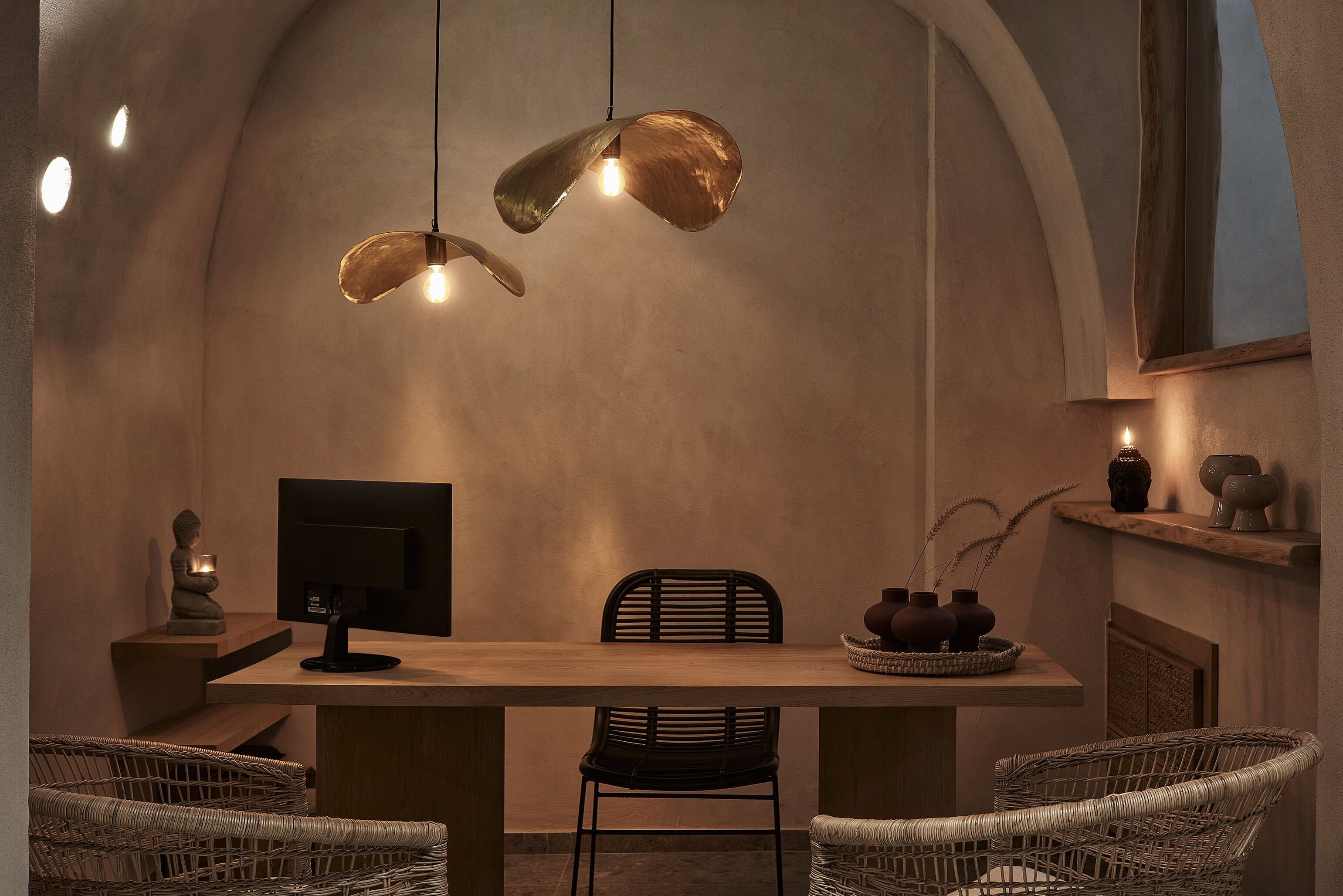 Un espace repas avec une longue table, des chaises en osier, une cheminée et des luminaires suspendus.