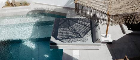 A pool area with a lounge chair and umbrella, a small table, and a chair.