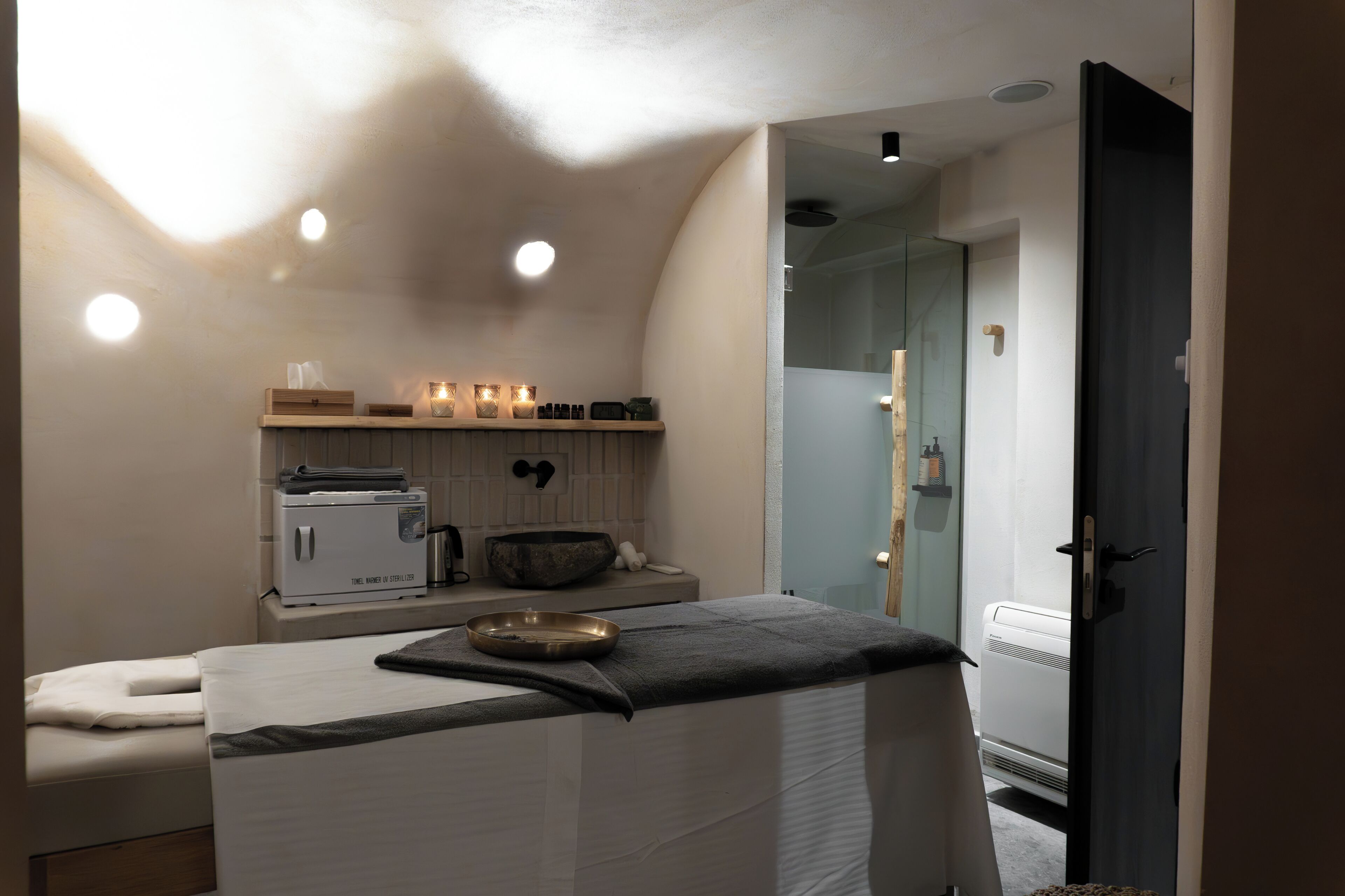 Habitación de spa con camilla de masaje, calentador de toallas y repisa con velas y aceites esenciales.