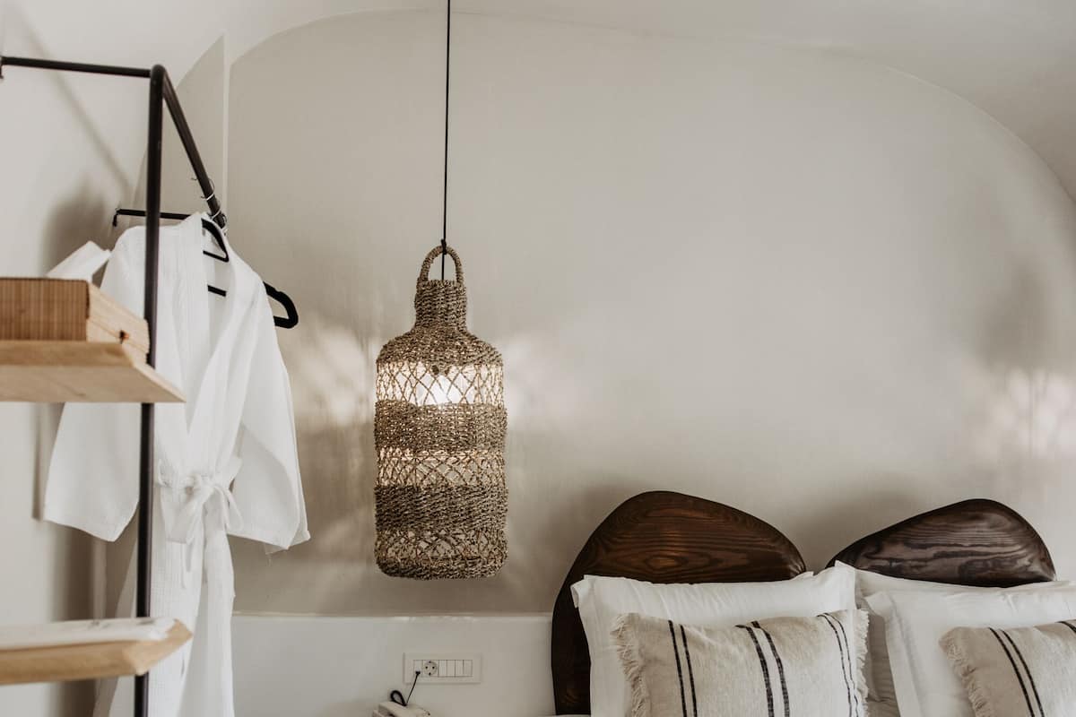 Un dormitorio con cama, mesita de noche, lámpara colgante y estante en la pared con bata y toalla.