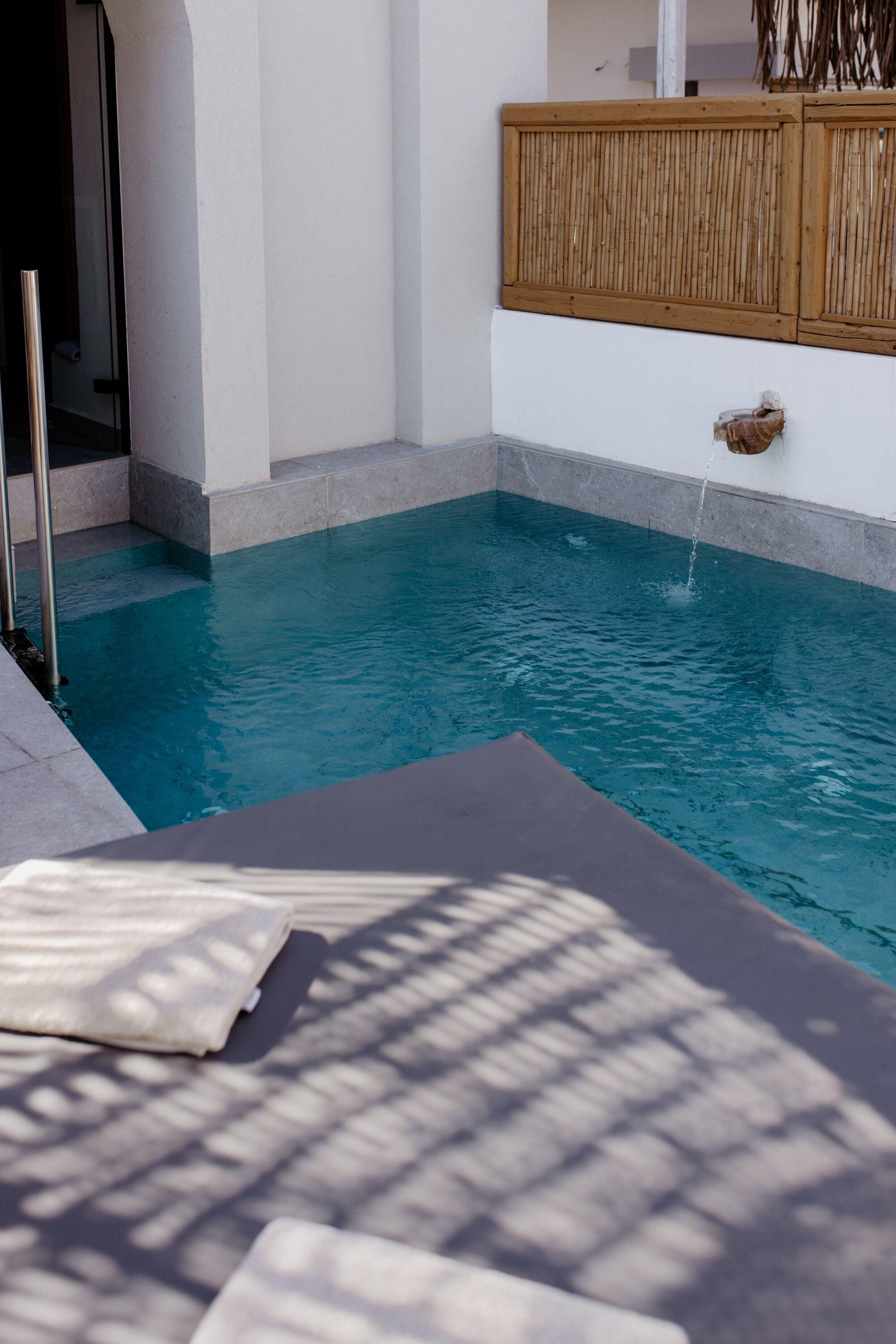 A pool area with a wooden deck, a lounge chair, and a water feature.