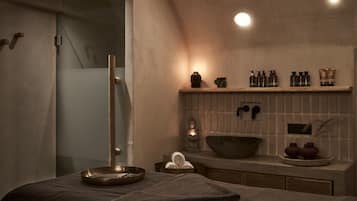 A modern bathroom with a glass shower enclosure, a wooden towel rack, a shelf with toiletries, and a stone basin.