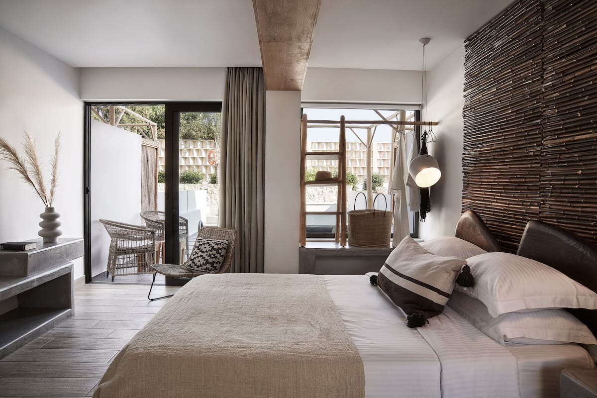 Un dormitorio moderno con una cama grande, vistas al exterior y una silla de mimbre junto a la ventana.