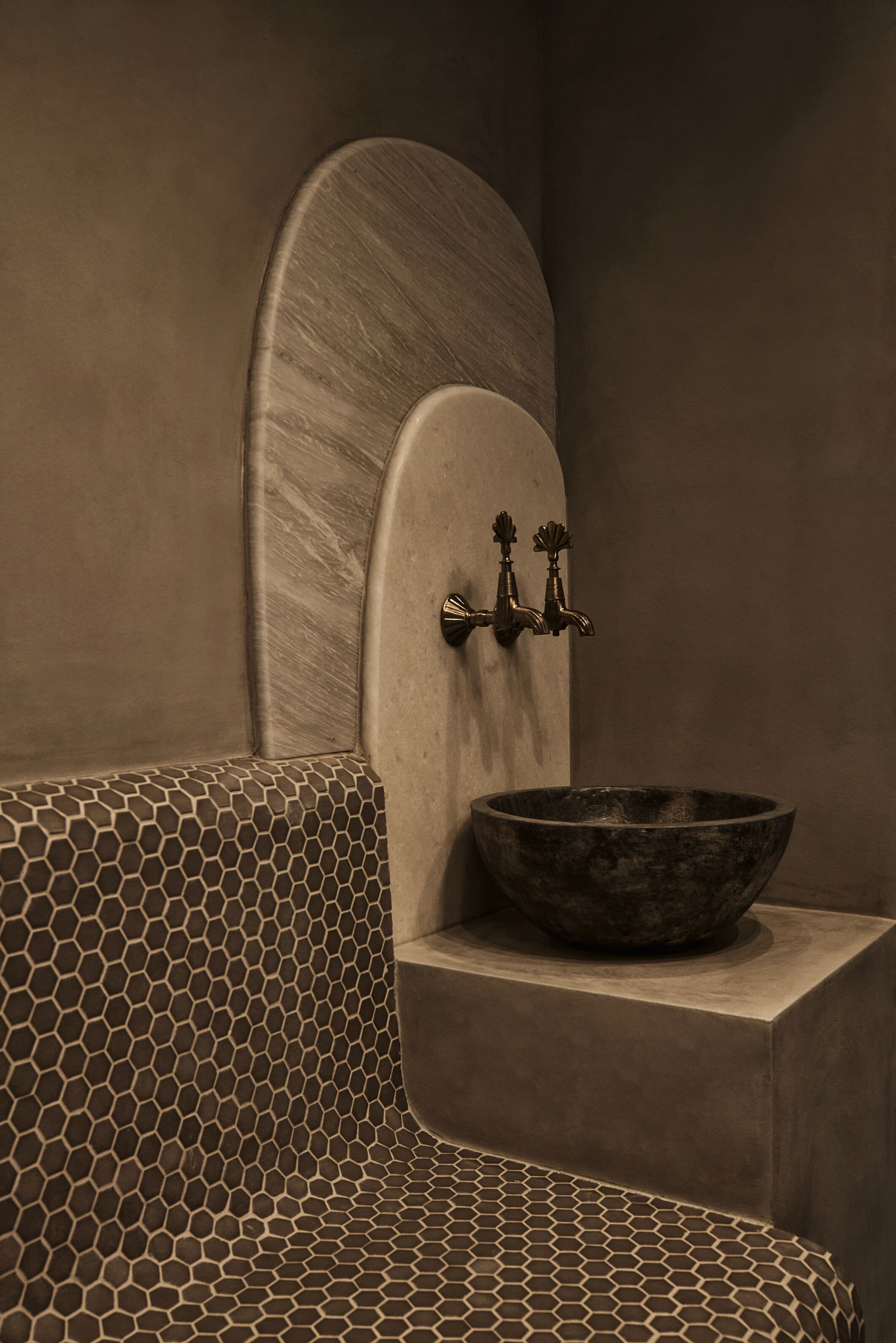 Ein Badezimmer mit einem sechseckig gemusterten Boden, einem Steingefäß und einem wandmontierten Wasserhahn.