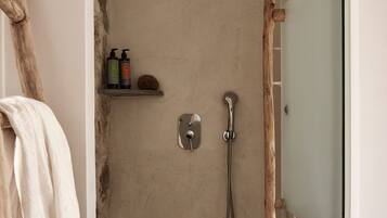 A bathroom with a shower, a towel rack, and a shelf with toiletries.