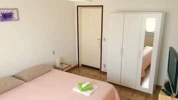 A bedroom with a bed, a wardrobe, a television, and a door leading to another room.