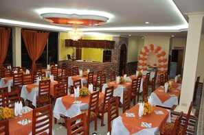 A restaurant with multiple tables, each set with white tablecloths and orange napkins. - Hotel El Caimito (Villavicencio)