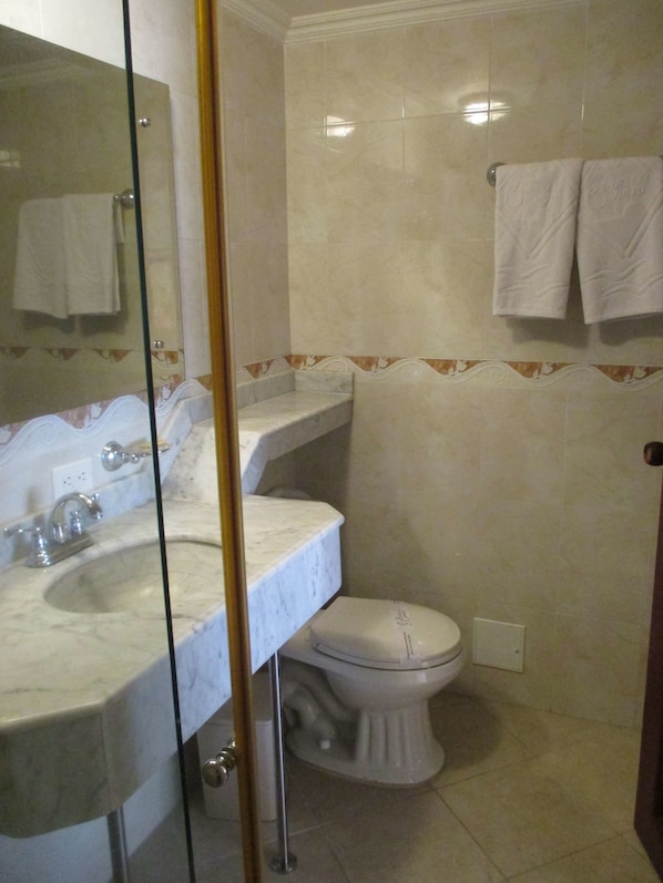 Un baño con lavamanos de mármol, inodoro y cabina de ducha de vidrio.