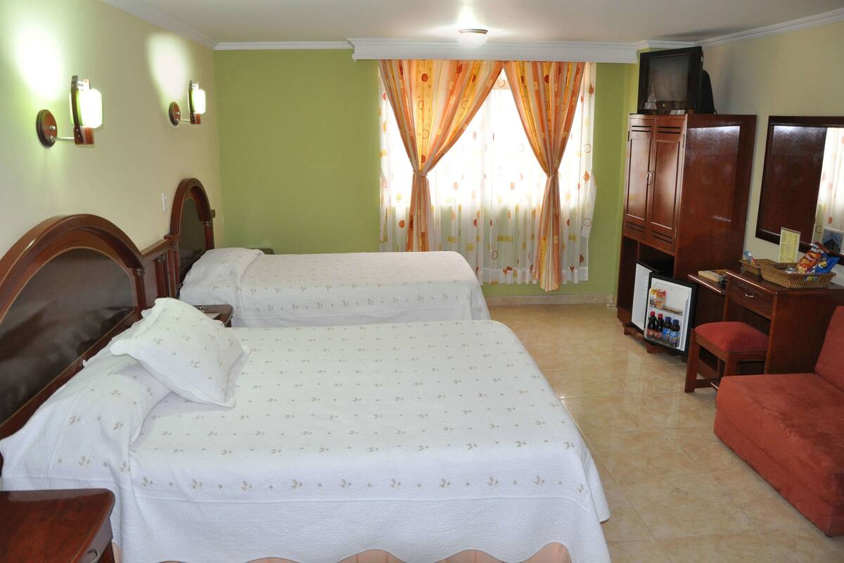 Una habitación de hotel con dos camas, televisión, una mesita y un refrigerador.