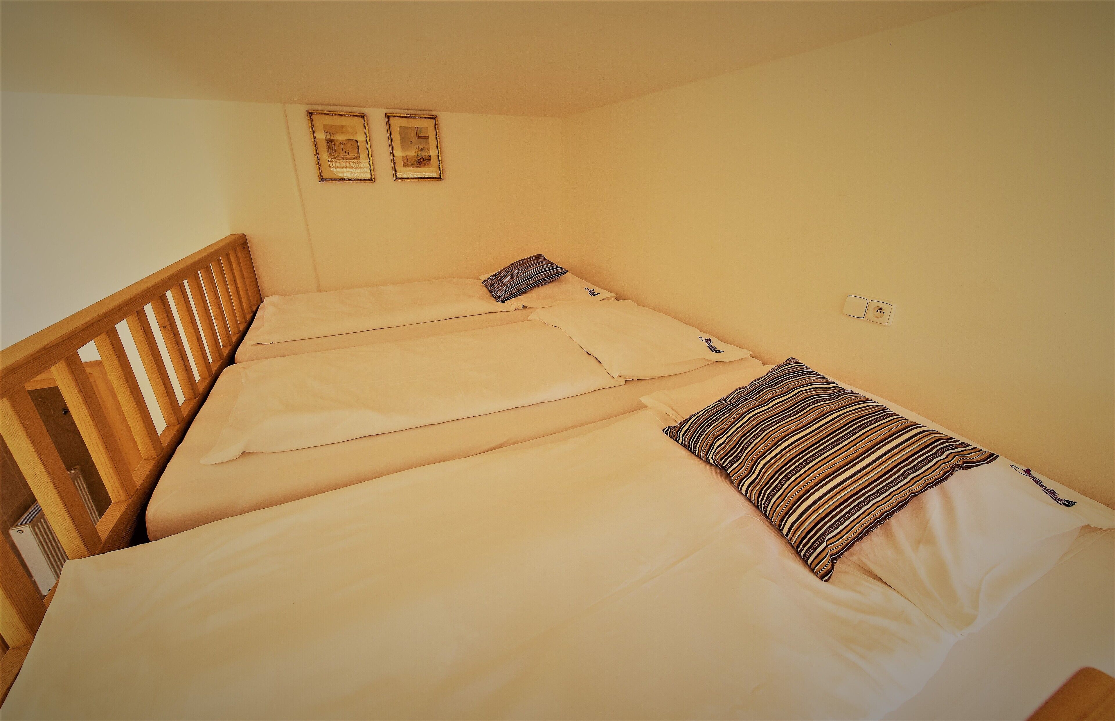 Een kleine kamer met een enkel bed, een houten hoofdbord, twee ingelijste foto's aan de muur en een stopcontact.