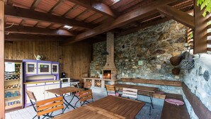 Un espacio de comedor al aire libre con mesas y bancos de madera, una pared de piedra y una chimenea de ladrillo.