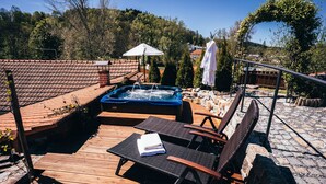 Una terraza de madera con un jacuzzi, sillas de descanso y un espacio cubierto con sombrillas.