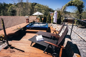 Una terraza de madera con un jacuzzi, sillas de descanso y un espacio cubierto con sombrillas.