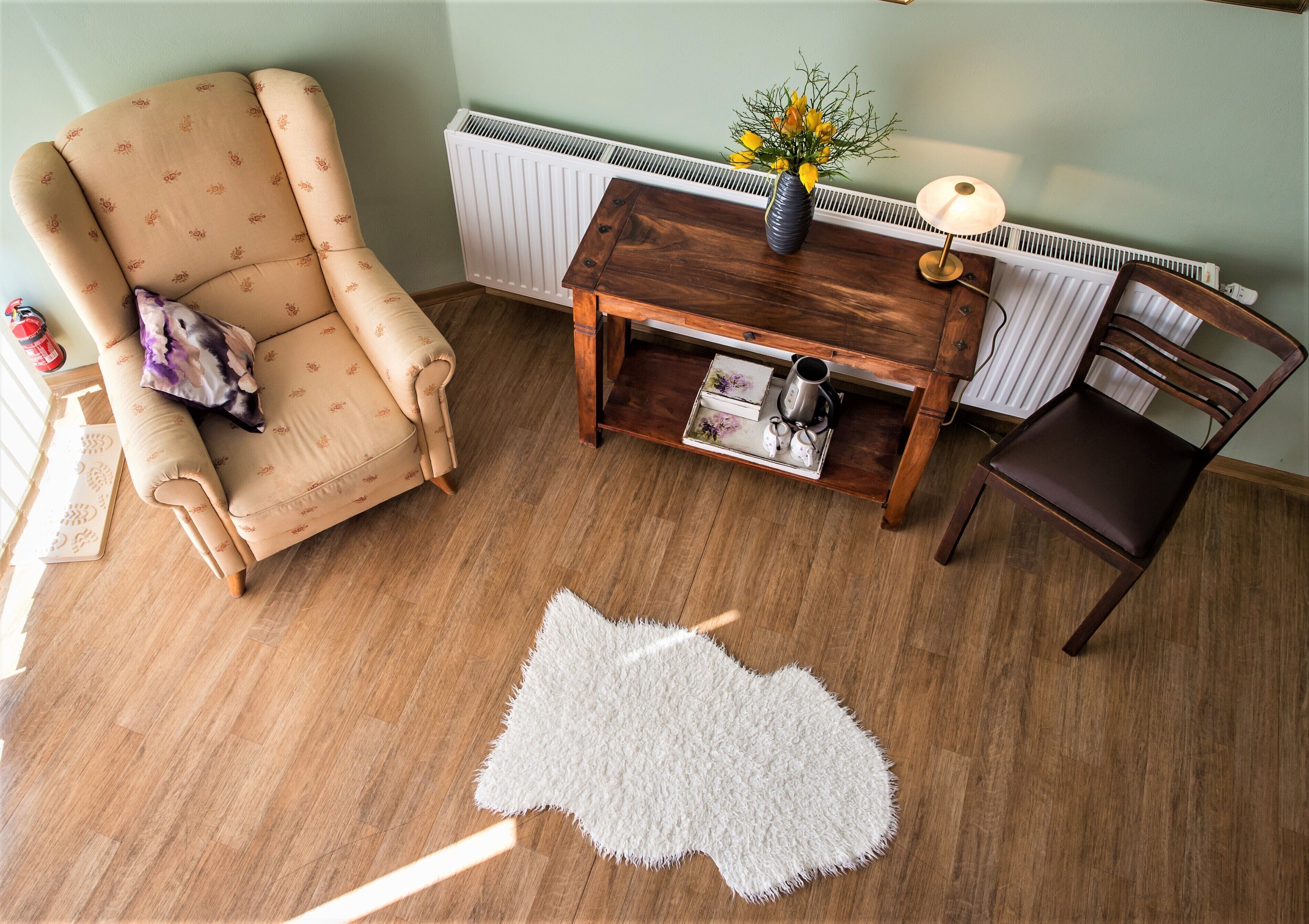 Una sala de estar acogedora con un sillón color beige, una mesa de centro de madera con un jarrón y una lámpara, y una alfombra blanca y mullida.