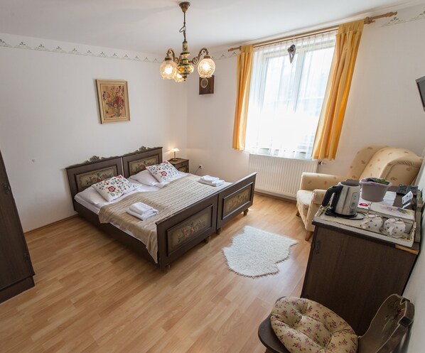 A bedroom with a wooden bed, a desk with a kettle, a chair, and a window with curtains. - Pension Fialka (Cesky Krumlov)