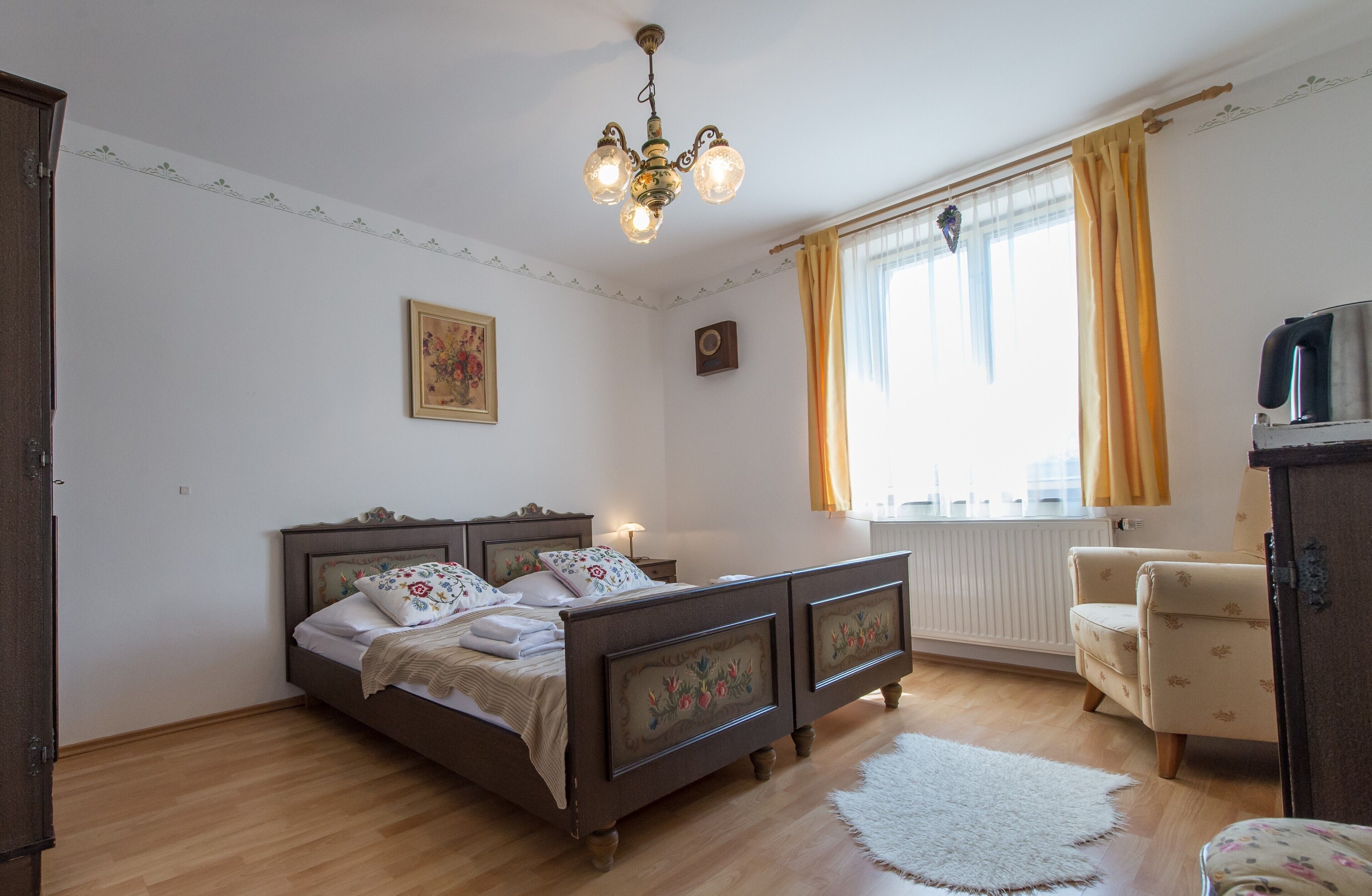 A bedroom with a wooden bed, a chair, a radiator, and a chandelier.