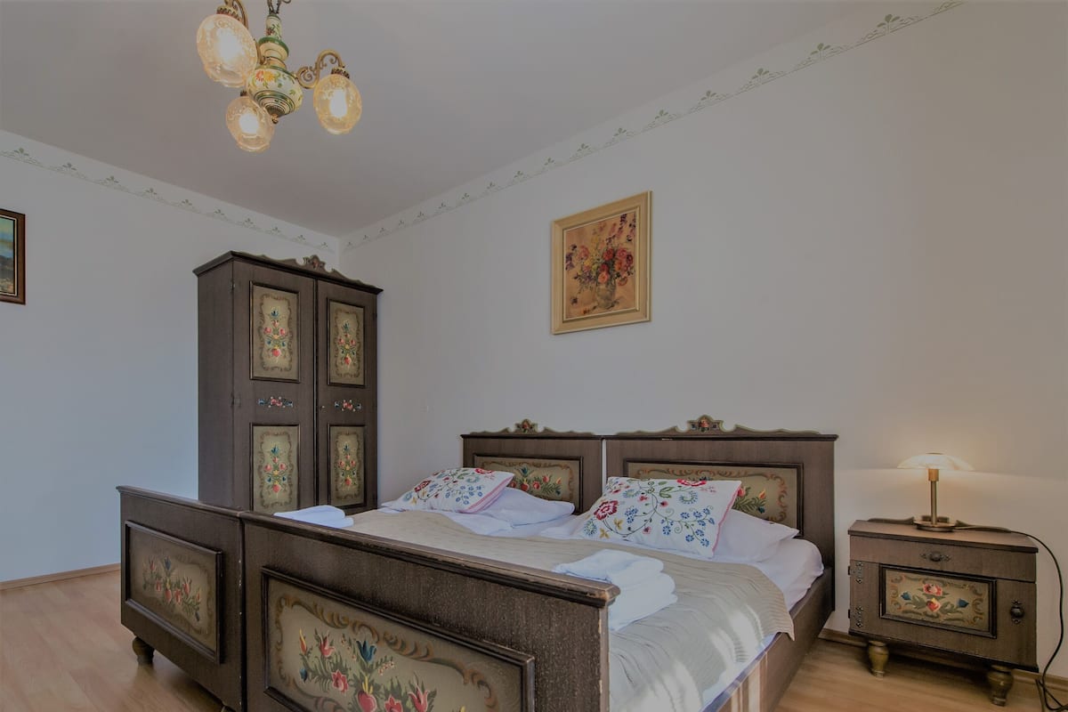 Um quarto com cama de madeira, mesa de cabeceira, cômoda e lustre.