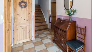 Una puerta de madera con un adorno de laurel, una escalera, un aparador, una silla y un espejo en la pared.