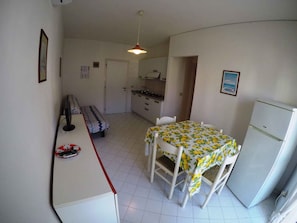 A compact kitchen with a dining table, chairs, a refrigerator, and a bench. - Holiday apartment near the beach (Rosolina Mare)