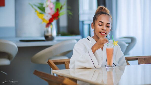 A person sitting at a table with a drink in front of them. - The Streamliner Hotel Apartment (Toamasina)
