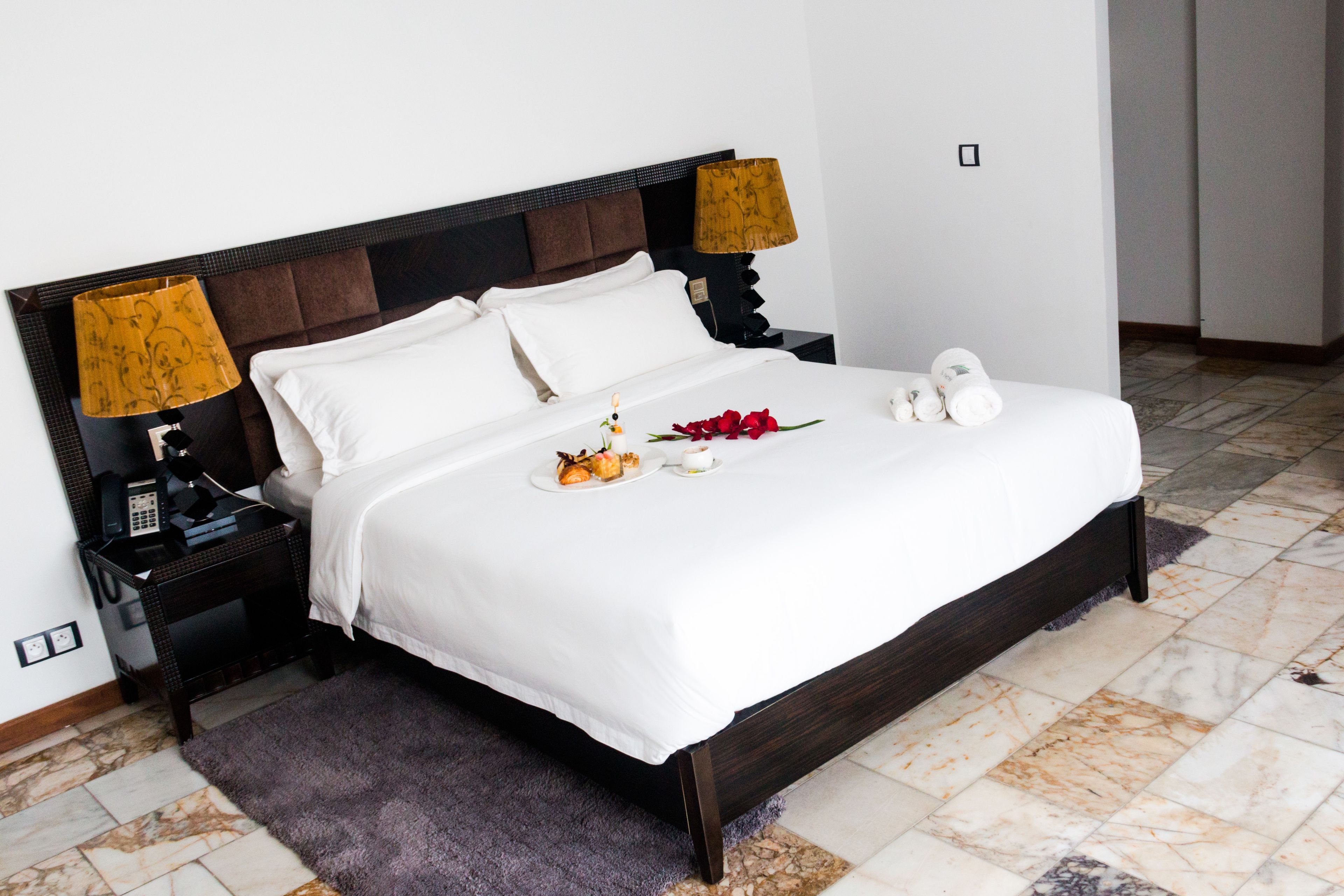 A neatly made bed with white linens, a dark wooden headboard, and two bedside lamps with yellow shades.