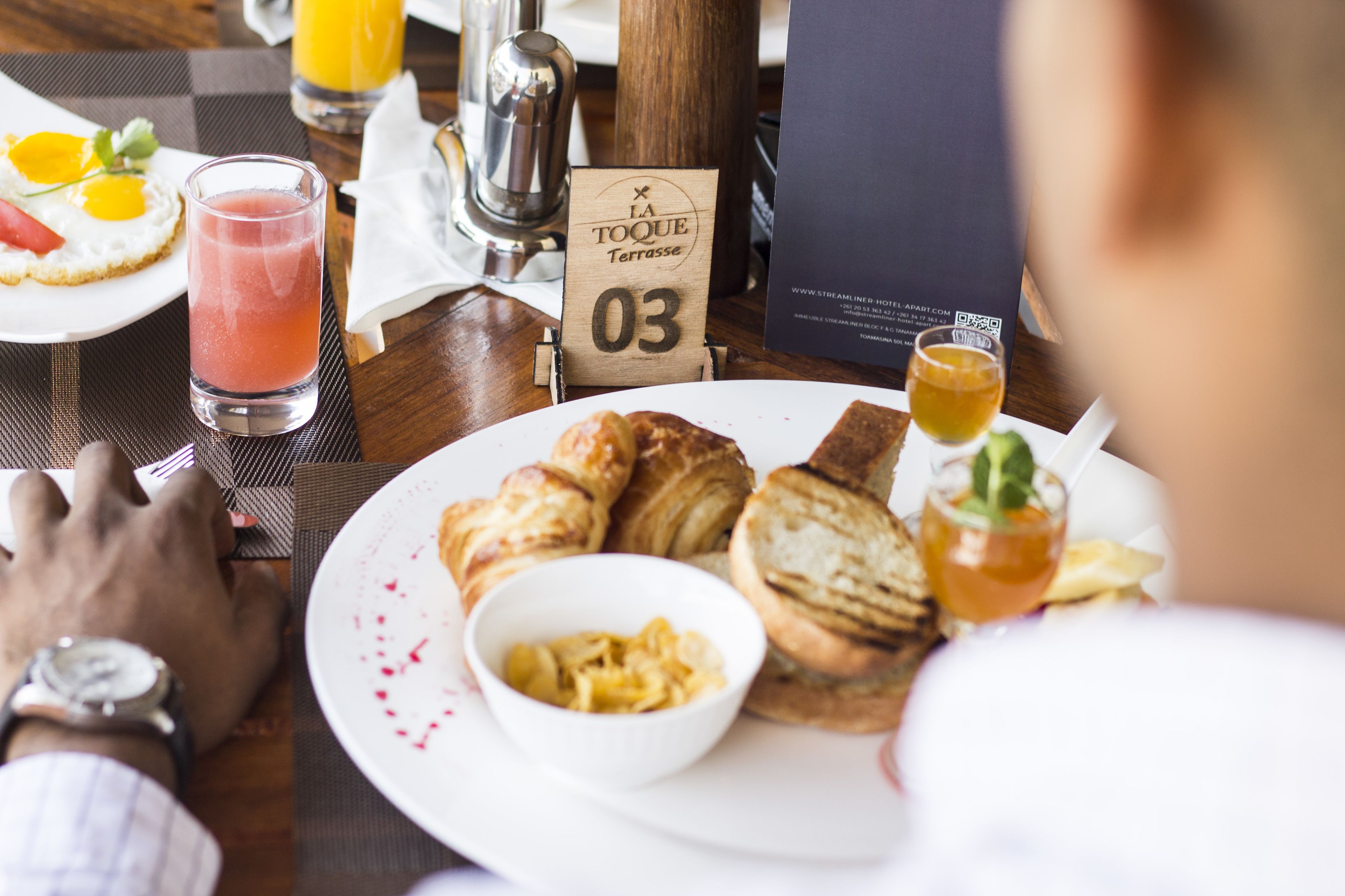 A breakfast setting with croissants, a bowl of scrambled eggs, and a glass of juice on a table.