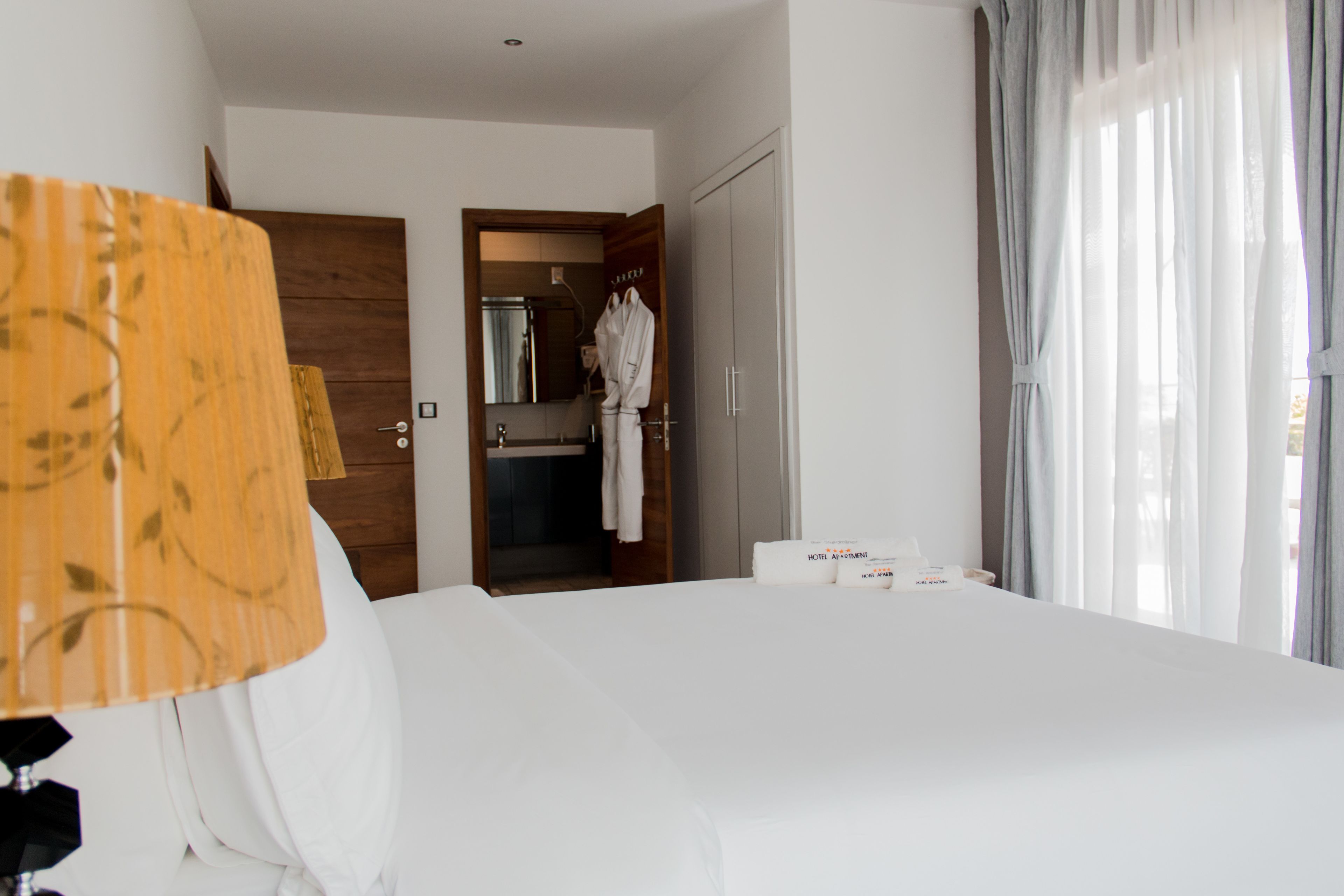 Una habitación de hotel con una cama grande, una puerta de madera, un baño con espejo y una ventana con cortinas.