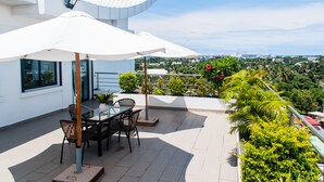 A terrace with a table and chairs, a white umbrella, and a view of the city. - The Streamliner Hotel Apartment (Toamasina)