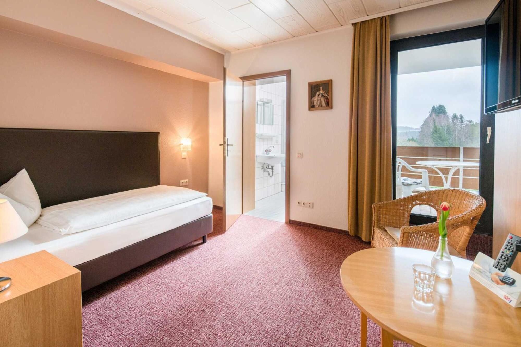 Ein Hotelzimmer mit Bett, einem kleinen Tisch, einem Stuhl, einem Fenster mit Blick und einer Tür zum Badezimmer.