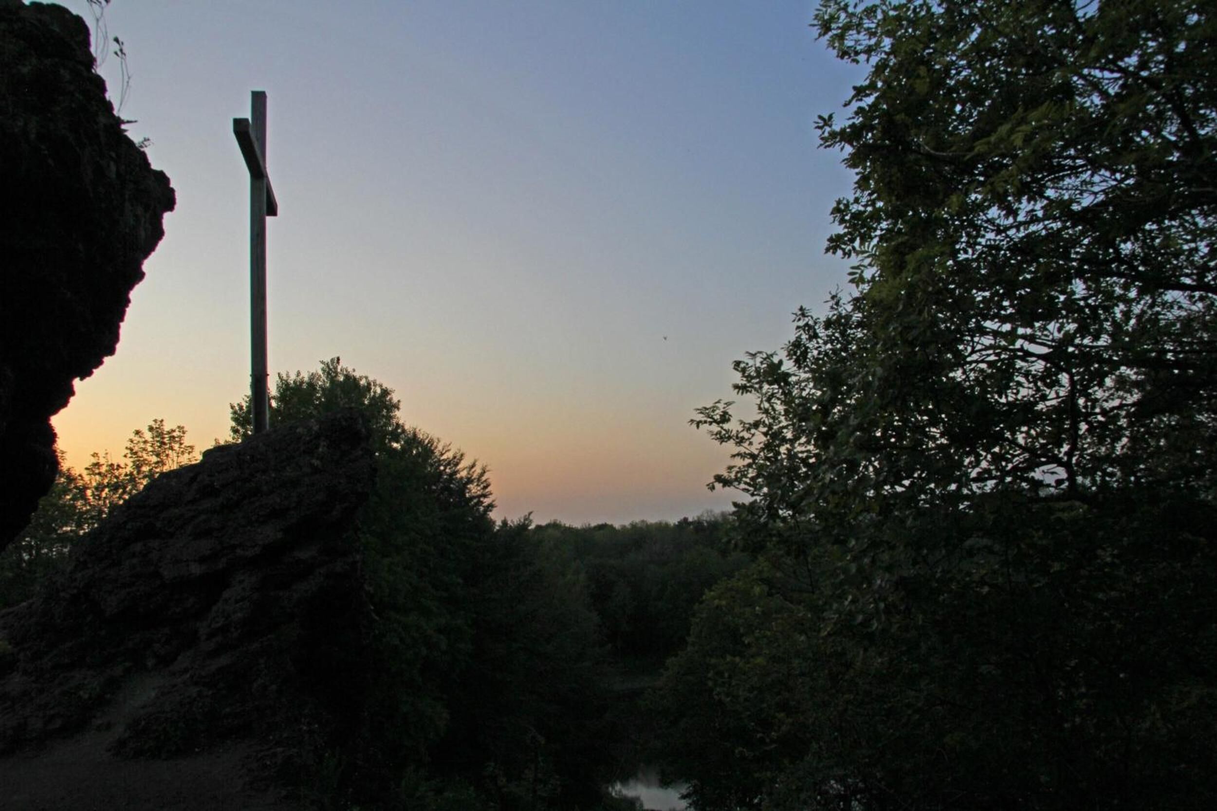 A cross in a natural setting with trees and a clear sky.