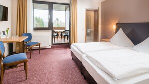 Habitación de hotel con cama, escritorio y silla, mesa con sillas y vista a un área exterior por una puerta.