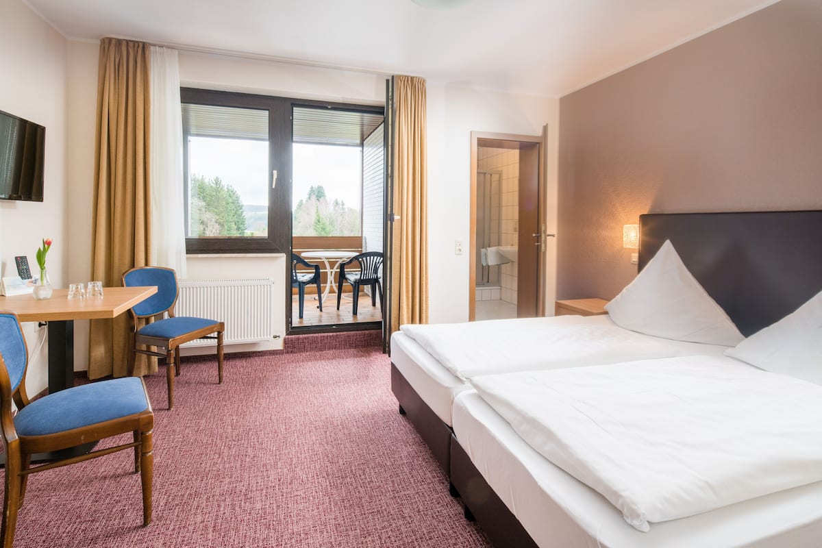 Habitación de hotel con cama, escritorio y silla, mesa con sillas y vista a un área exterior por una puerta.