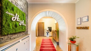 Un pasillo de hotel con alfombra roja, una recepción y una pared con un cartel verde.