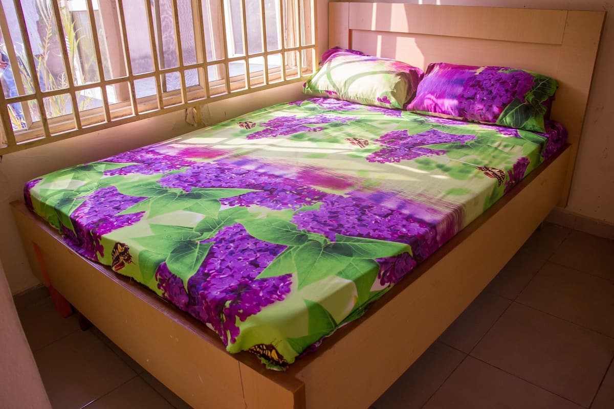 A bed with a floral bedspread, wooden headboard, and a window with bars.