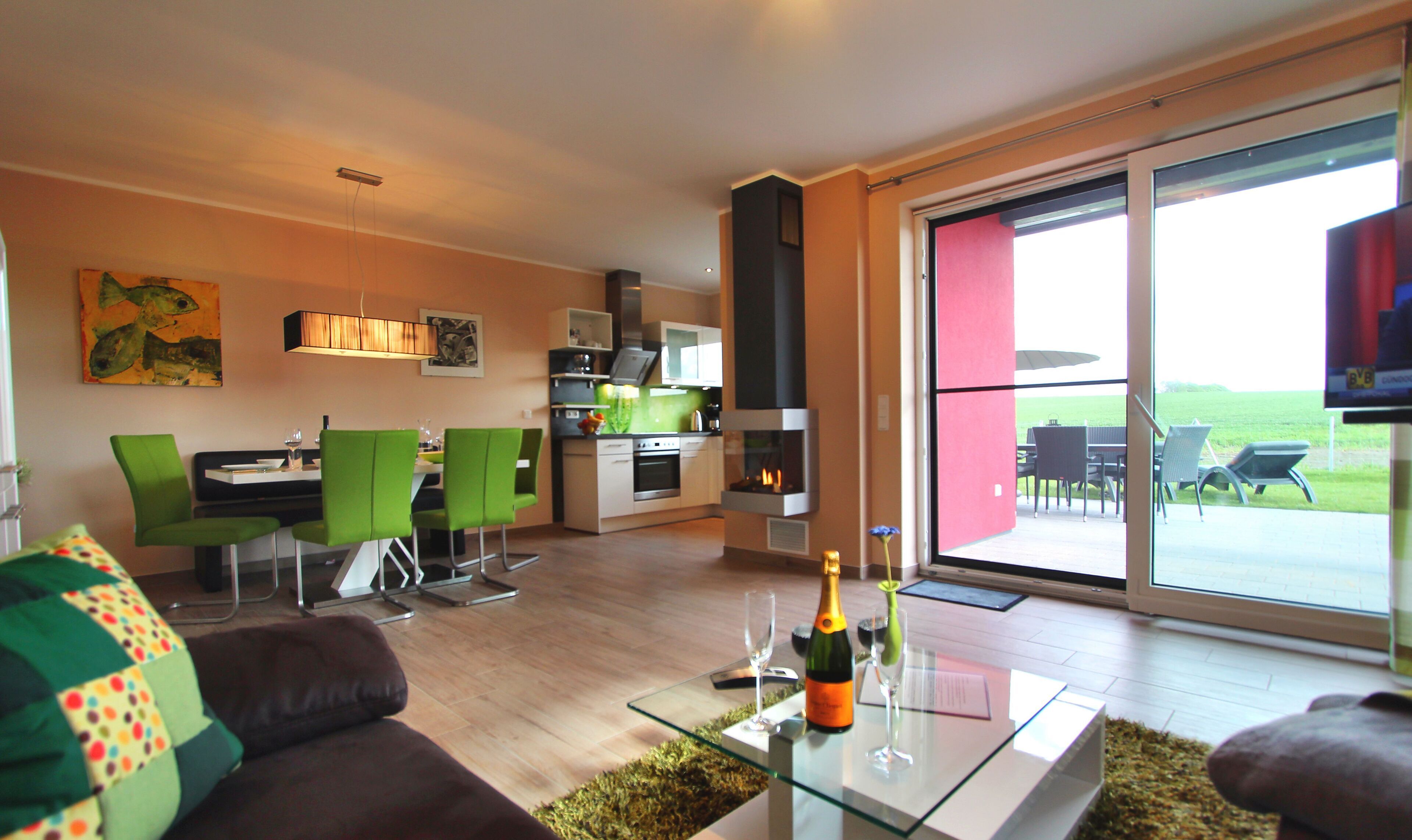 A modern living room with a glass coffee table, a sofa, and a dining area with green chairs.