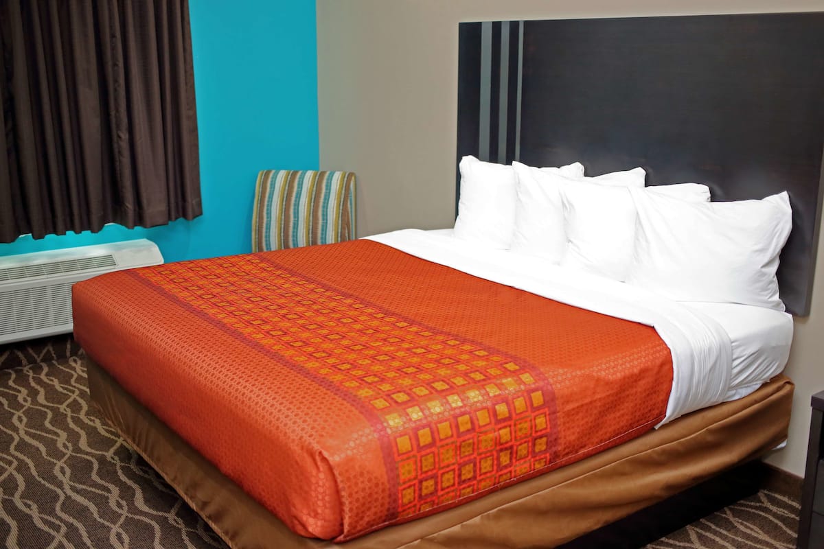 A hotel room with a bed, a striped chair, a wall-mounted air conditioner, and a patterned carpet.