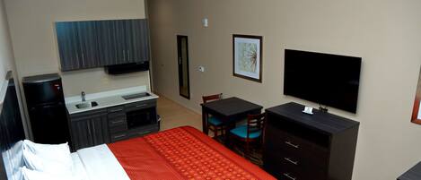 Une chambre d’hôtel équipée d’un lit, d’un bureau, d’une chaise, d’une télévision, d’une armoire et d’une petite kitchenette.