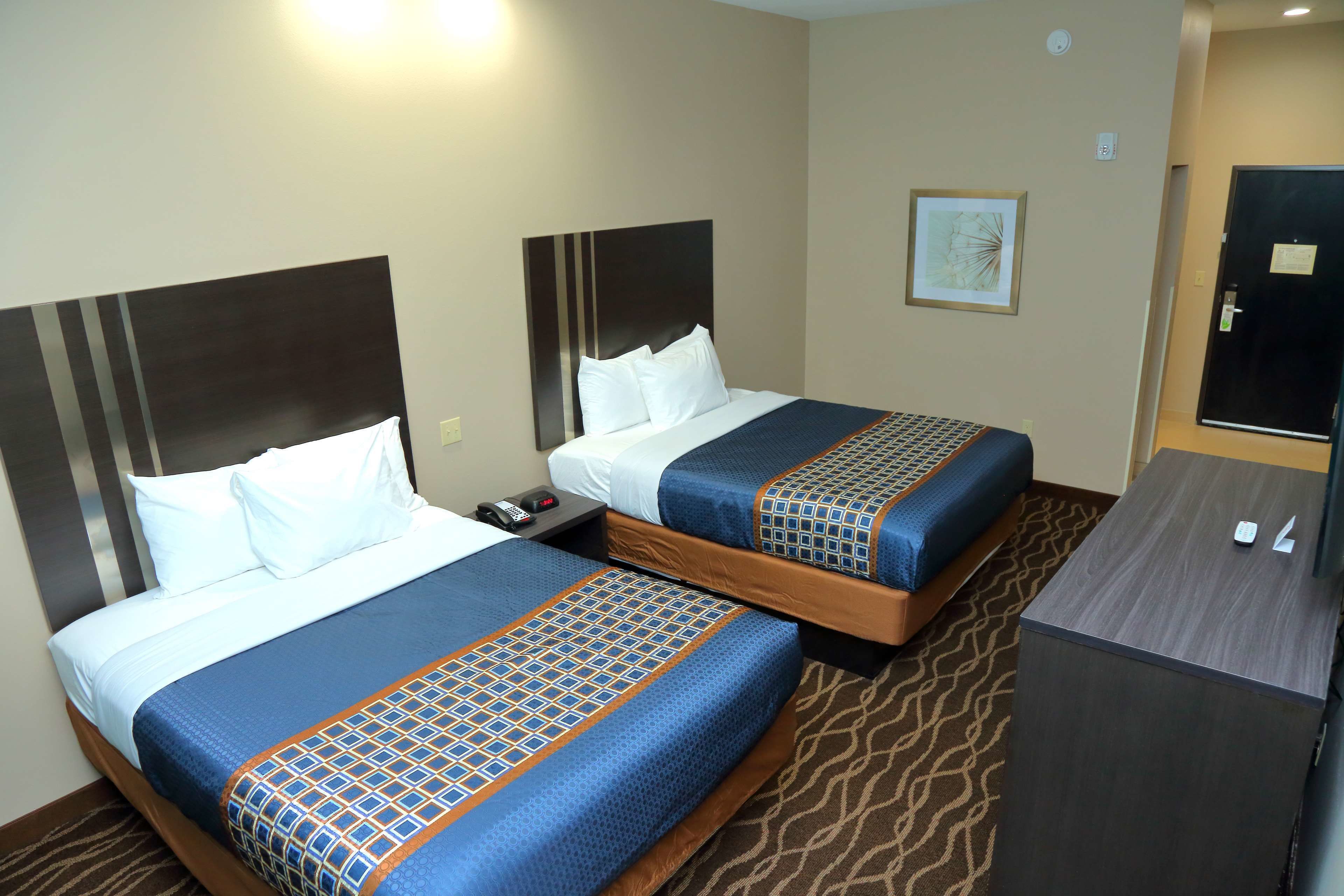 A hotel room with two beds, each with a patterned bedspread, a nightstand, and a desk with a chair.