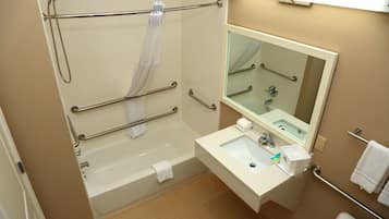 A bathroom with a bathtub, a sink, a mirror, and handrails.