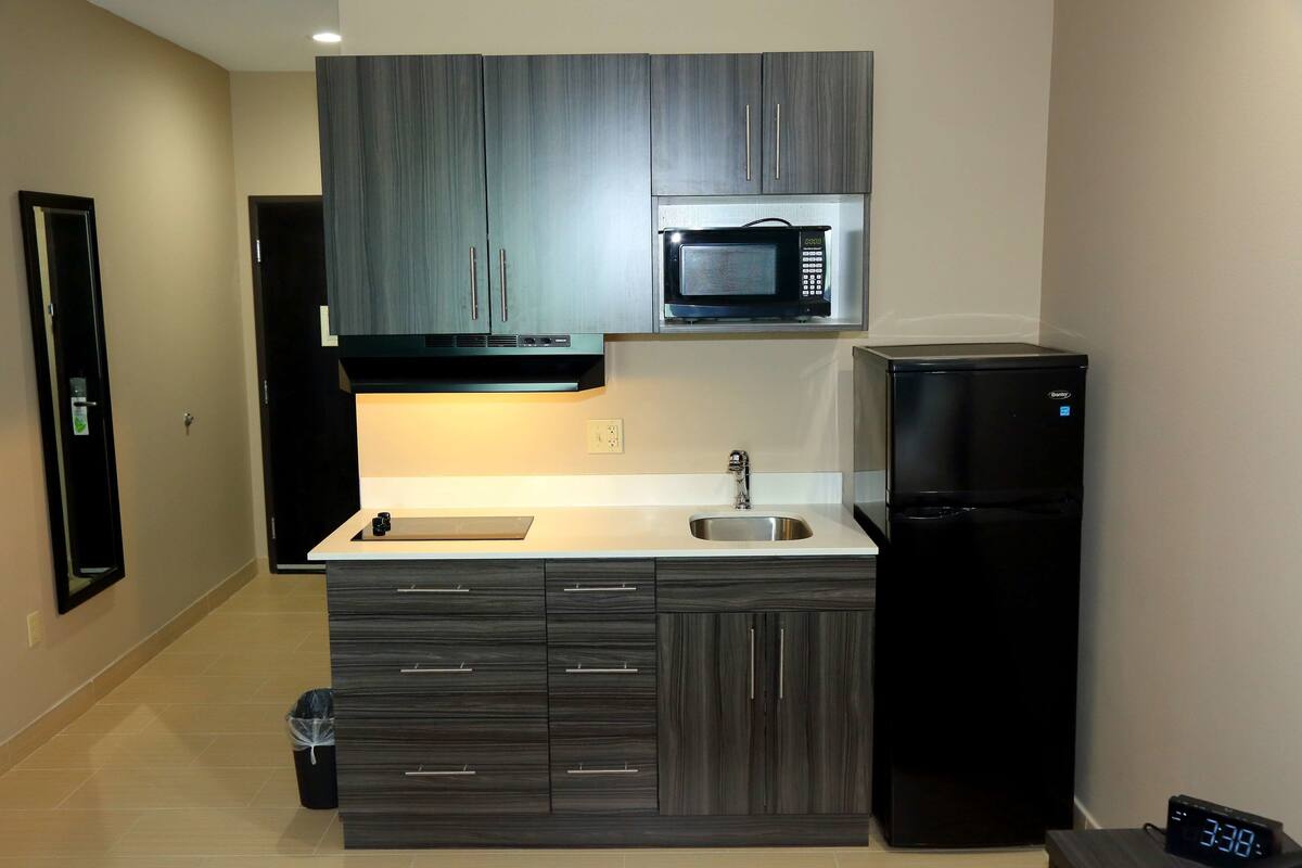 A modern kitchen with dark wood cabinets, a stainless steel microwave, a black refrigerator, and a sink.