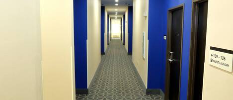 A hotel hallway with blue walls and a patterned carpet. There is a sign indicating guest laundry rooms at the end.