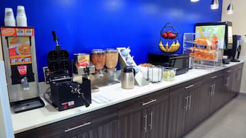A breakfast bar with a coffee machine, waffle maker, and various food containers.