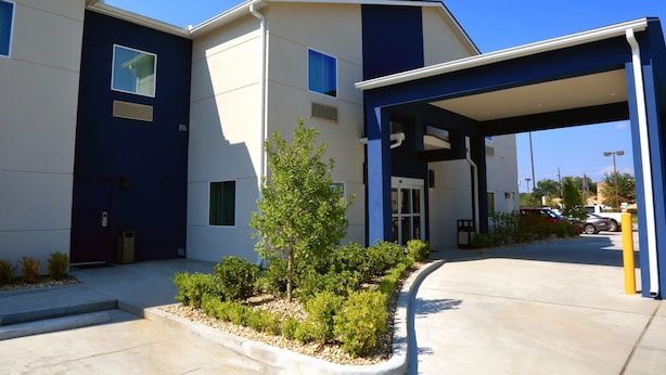 A modern building with a covered entrance, a small tree, and a parking area. - Americas Best Value Inn & Suites Prairieville (Prairieville)
