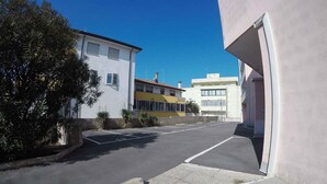 A parking lot with a building on the left and a white building on the right.
