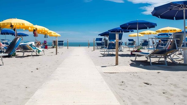 A beach with rows of sun loungers and umbrellas, a wooden walkway, and the ocean in the background.