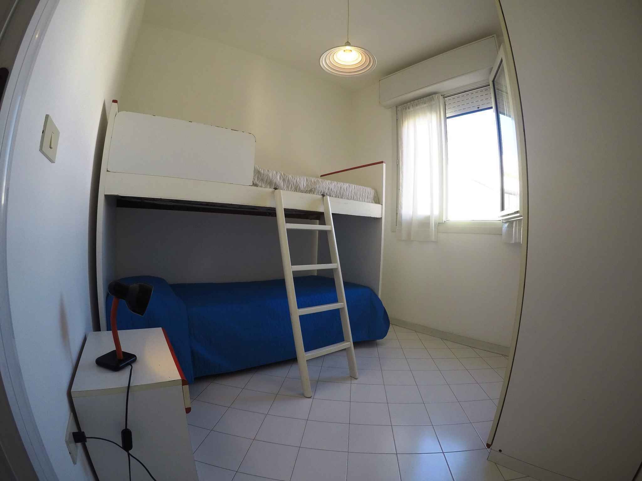 A small, single-bedded room with a bunk bed, a ladder, a desk with a chair, and a window with curtains.