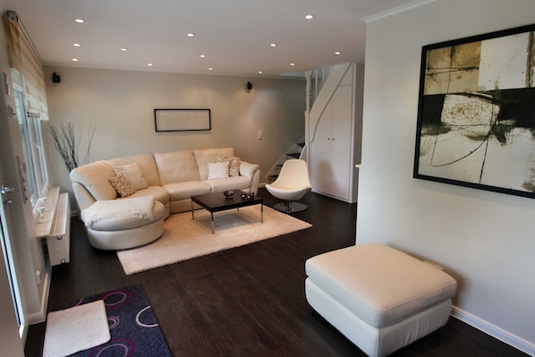A modern living room with a white sofa, a coffee table, and a white armchair. There is a staircase leading to another level.