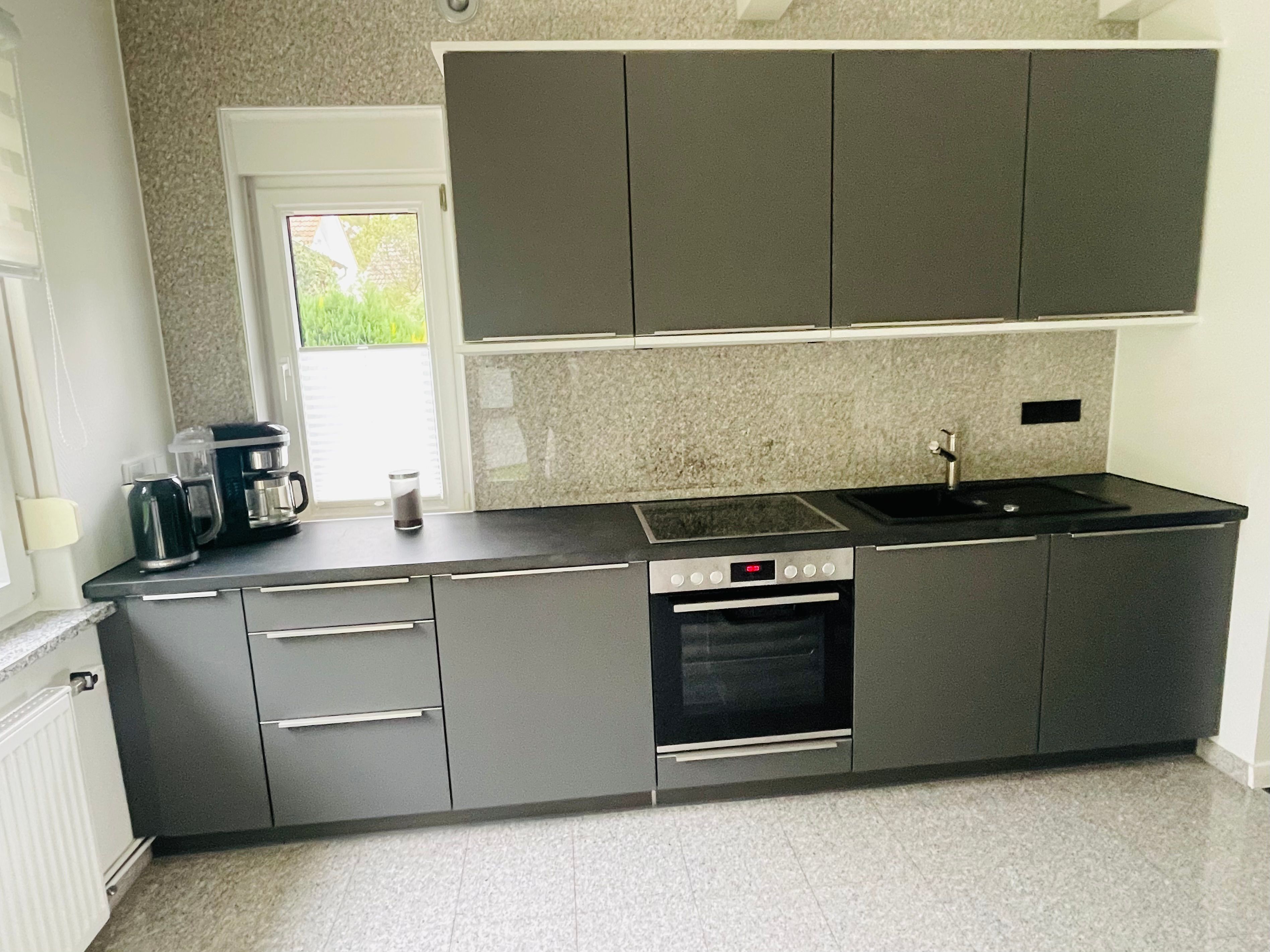 Eine moderne Küche mit grauen Schränken, einem eingebauten Ofen und einer Spüle.